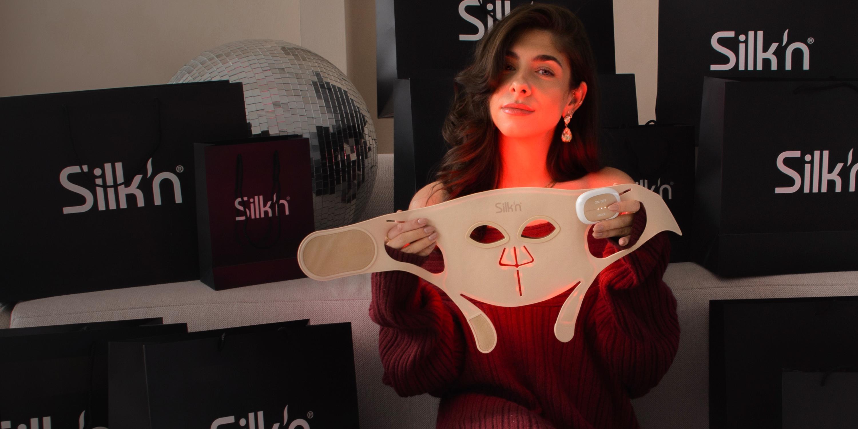 Vrouw zit tussen de geschenkjes en toont haar favoriete Black Friday promo en cadeautip voor kerst: LED Face Mask Pro van Silk'n