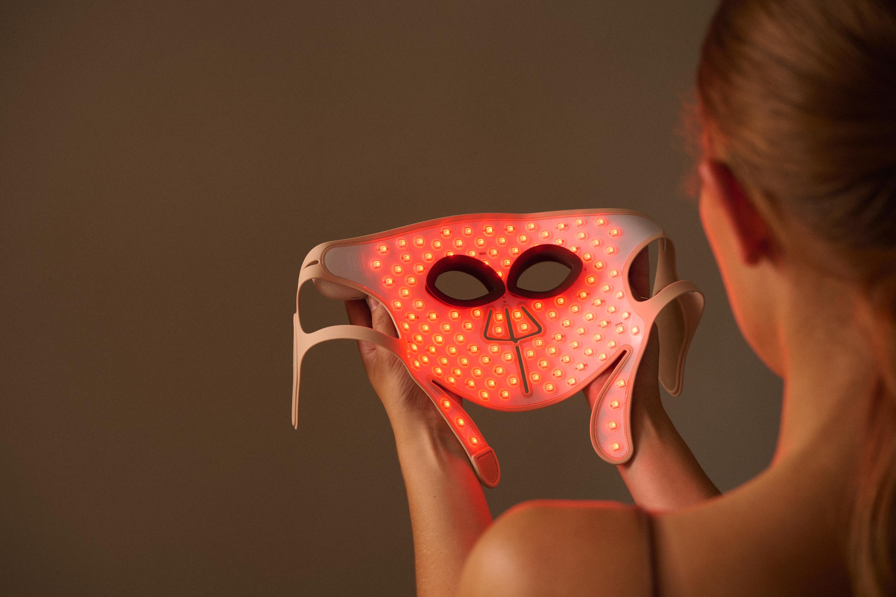 Woman holding the LED Face Mask Pro from Silk'n with red lights showing at the inside of the mask