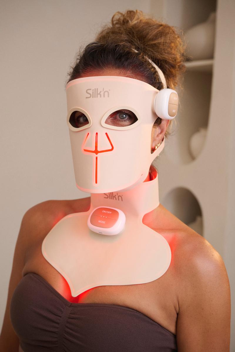 Frau beim Anlegen der LED Face Mask Pro und LED Chest Mask &ndash; kombiniert Rotlichttherapie mit der innovativen Caeli-Linsentechnik.
