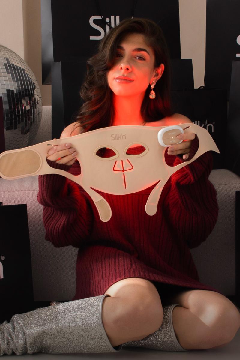 Vrouw zit tussen de geschenkjes en toont haar favoriete Black Friday promo en cadeautip voor kerst: LED Face Mask Pro van Silk'n