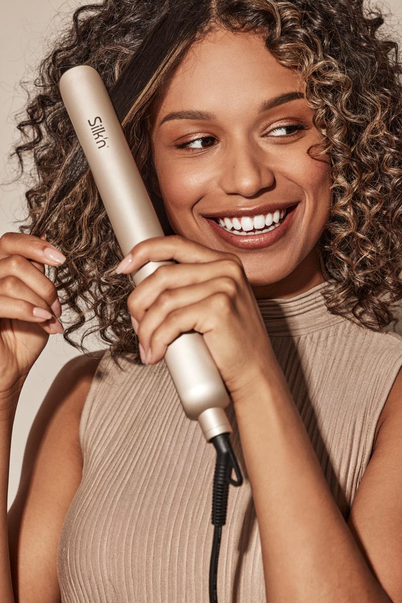Smiling woman using the Silk'n SilkyStraight hair straightener on her curly hair
