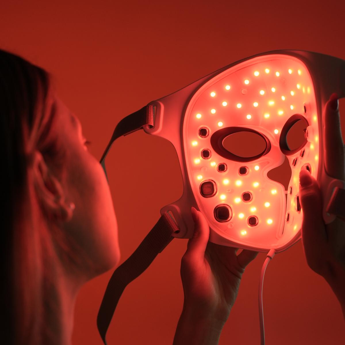 Une femme observe la technologie LED (rouge) et EMS &agrave; l'int&eacute;rieur du masque avant de le mettre